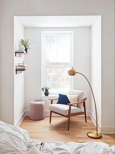 a bedroom with white walls and wooden floors, a chair in front of a window