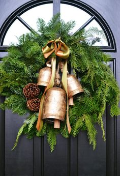 a wreath with bells and pine cones hanging from the front door is adorned with evergreen leaves