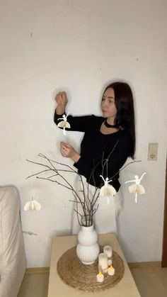 a woman standing next to a white vase with flowers in it on top of a table