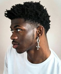 a young man with an afro wearing earrings and a white t - shirt is looking off to the side