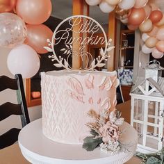 there is a pink cake on the table with balloons in the background and decorations around it