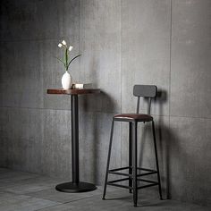 two stools are next to a table with a vase on it and a flower in the middle