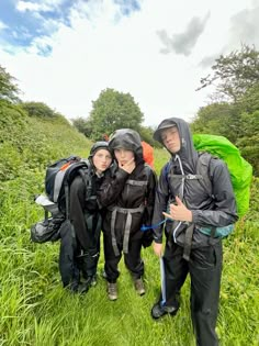 three people with backpacks standing in the grass