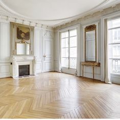 an empty room with wooden floors and white walls, large mirrors on either side of the fireplace