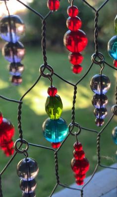 colorful glass beads hang from a chain link fence in front of a grassy area with trees