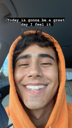 a young man wearing an orange hoodie smiles at the camera while sitting in his car