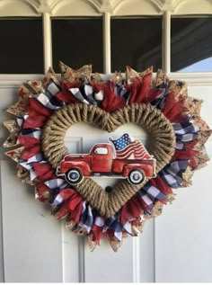 a heart shaped wreath with an old red truck and american flag on the front door