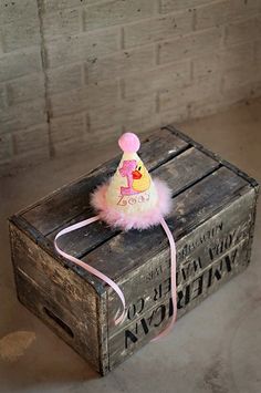 a small pink hat sitting on top of an old wooden box with a string attached to it