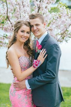 a young man and woman in formal wear posing for a photo under the blossomy tree