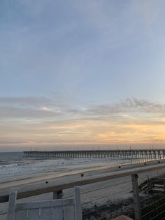 a bench sitting on top of a sandy beach next to the ocean with a pier in the background