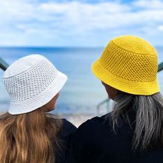 two women looking out at the ocean while wearing yellow and white hats on their heads