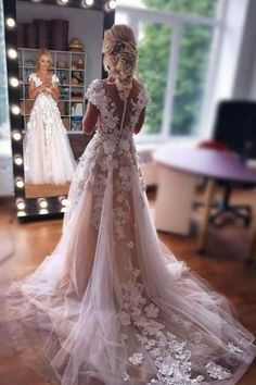 a woman standing in front of a mirror wearing a wedding dress with flowers on it