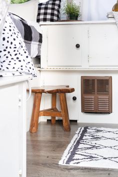 a white dresser with black and white pillows on it's top shelf next to a wooden stool