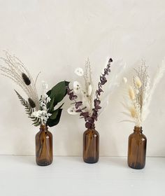 three brown glass vases with flowers in them