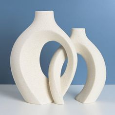 two white vases sitting next to each other on a blue background with one in the foreground