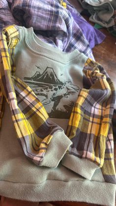 several plaid shirts are stacked on top of each other, with mountains in the background