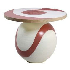 a white and red vase sitting on top of a wooden table topped with a circular object