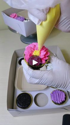 someone in white gloves is decorating cupcakes with pink and yellow icing