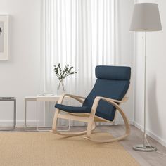 a green rocking chair sits in front of a white wall with curtains and a lamp