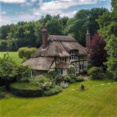 an aerial view of a thatched roof house in the middle of a lush green field