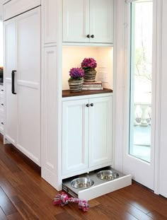 a kitchen with white cabinets and dog bowls on the floor next to an open door