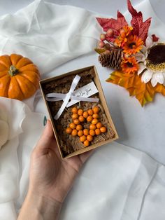 a person holding a box with candy in it on a white blanket next to flowers and pumpkins