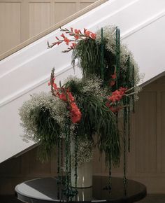 some flowers are in a white vase on a table under the bannister stairs