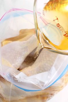 a person pouring liquid into a bowl filled with chicken breast fillers on top of a table