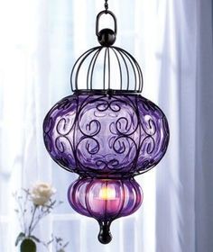 a purple lamp hanging from a ceiling in front of a window with curtains and flowers