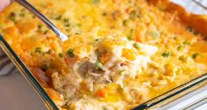 a person holding a spoon over a casserole dish with chicken and vegetables in it