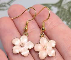 Introducing our Pink Cherry Blossom Earrings, a pair of delicate and elegant accessories that capture the beauty of blooming spring flowers. These earrings feature soft pink cherry blossoms, each meticulously designed to add a touch of grace and charm to your look. The gold stainless steel hooks offer a sophisticated finish while ensuring durability and comfort. The dainty design makes these earrings perfect for both everyday wear and special occasions, adding a subtle yet refined touch to any outfit. Ideal for those who appreciate elegant, nature-inspired jewelry, these Pink Cherry Blossom Earrings make a beautiful addition to your collection or a thoughtful gift for someone special. Embrace the elegance of spring all year round with these enchanting earrings. Cherry Blossom Earrings, Nature Inspired Accessories, Pink Cherry Blossom, Jewelry Elegant, Accessories Gold, Floral Jewelry, Pink Cherry, Nature Inspired Jewelry, Floral Jewellery