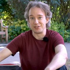 a man sitting on the ground in front of a park bench with his legs crossed