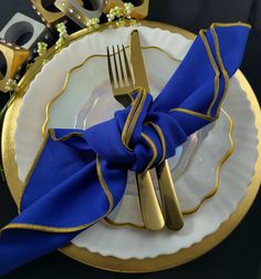 a blue and gold place setting on a white plate with a fork, knife and napkin