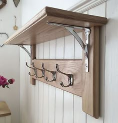 a wooden shelf with hooks on it and flowers in the vase next to it,