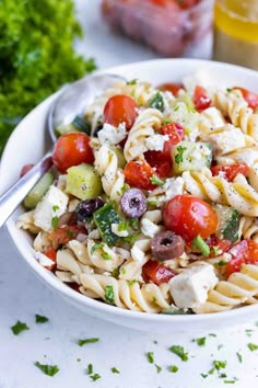 a white bowl filled with pasta salad next to a glass of orange juice and parsley