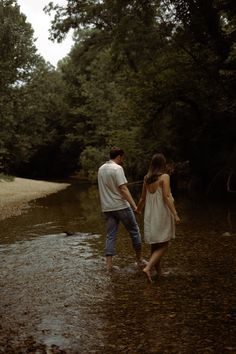 a man and woman walking in the water holding hands while they are standing next to each other