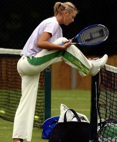 a female tennis player leaning on the net with her racket in hand while waiting for the ball to be hit