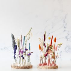 two vases filled with different types of flowers on top of a white table next to each other