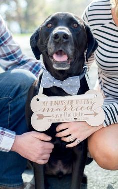 a black dog wearing a bow tie and holding a wooden sign