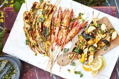 several skewers of food on a cutting board with lemon wedges and parsley