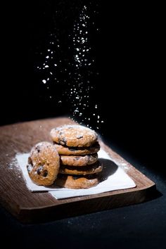 chocolate chip cookies are sprinkled with powder on a wooden cutting board in the dark