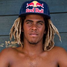 a shirtless man with dreadlocks and a red bull hat on his head