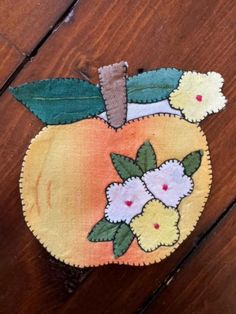 an apple with flowers on it sitting on top of a wooden floor next to a piece of cloth