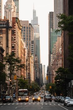 a city street filled with lots of tall buildings next to trees and cars driving down it