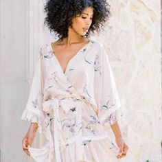 a woman wearing a white dress with flowers on it and an afro hairstyle standing in front of a wall