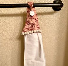 a white towel hanging on a black bar with a button in the middle and a pink knitted hat attached to it