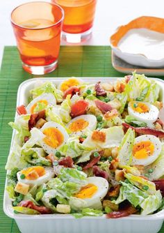 a salad with hard boiled eggs and bacon in a white bowl on a green place mat