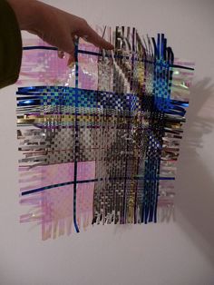 a person holding up a piece of art made out of strips of colored paper and duct tape