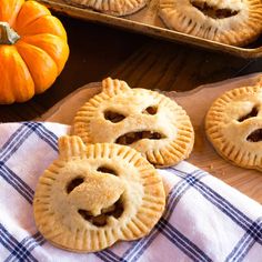 three small pies with faces on them sitting on a table next to some pumpkins