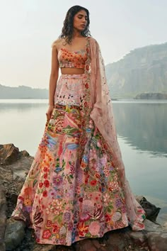 a woman standing on top of a rock next to a lake wearing a colorful dress